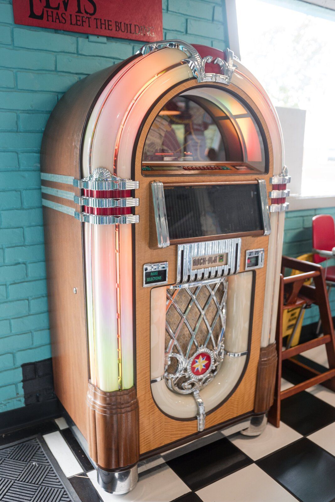 A lit-up jukebox against a teal brick wall