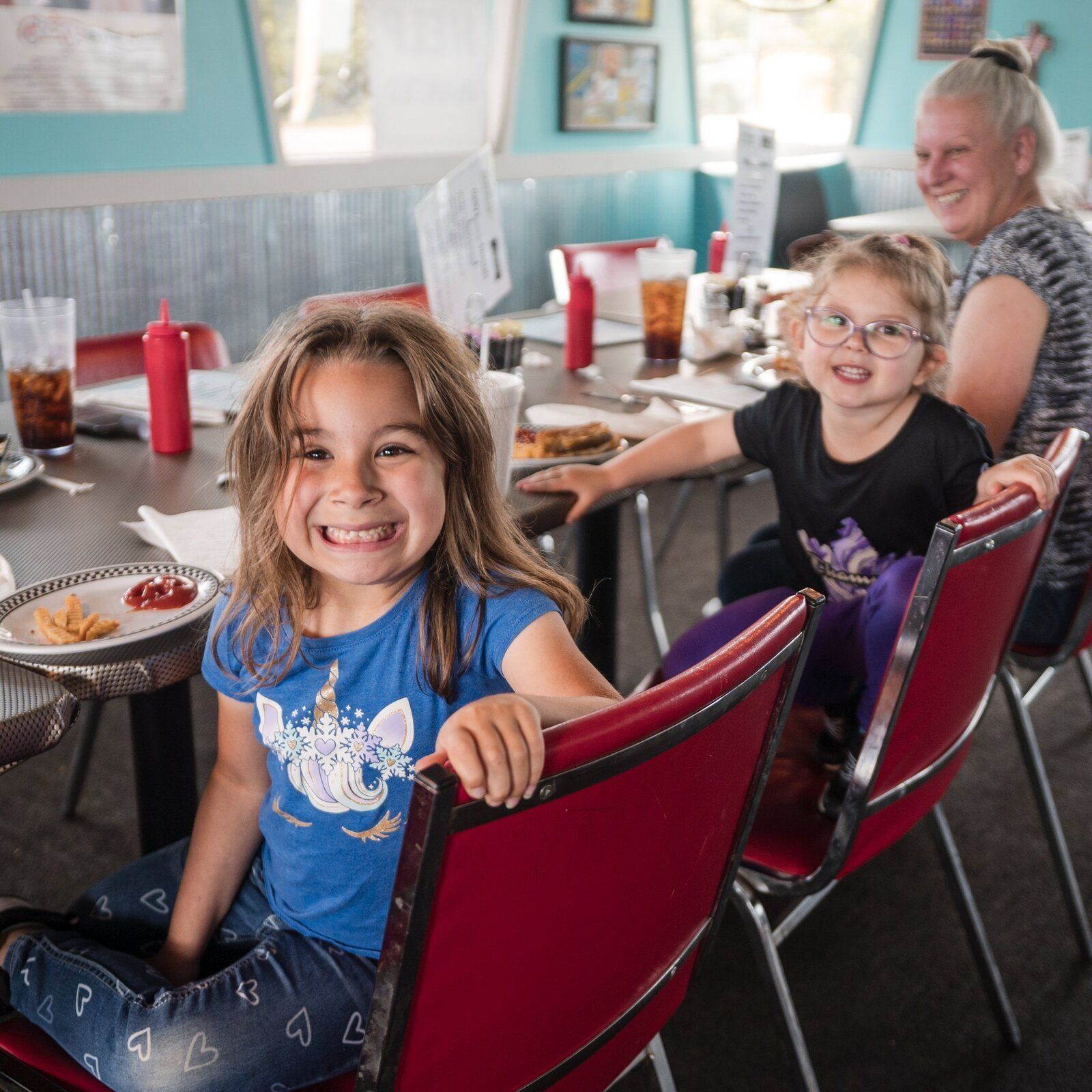 Two kids grinning in the cherry-red chairs