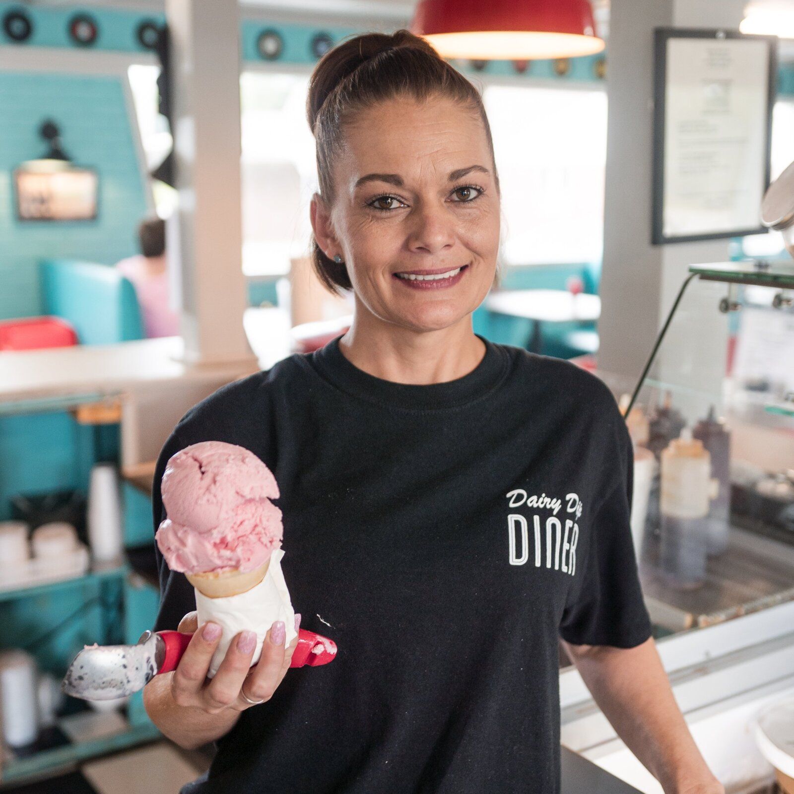 A smiling server holding up a strawberry ice cream cone